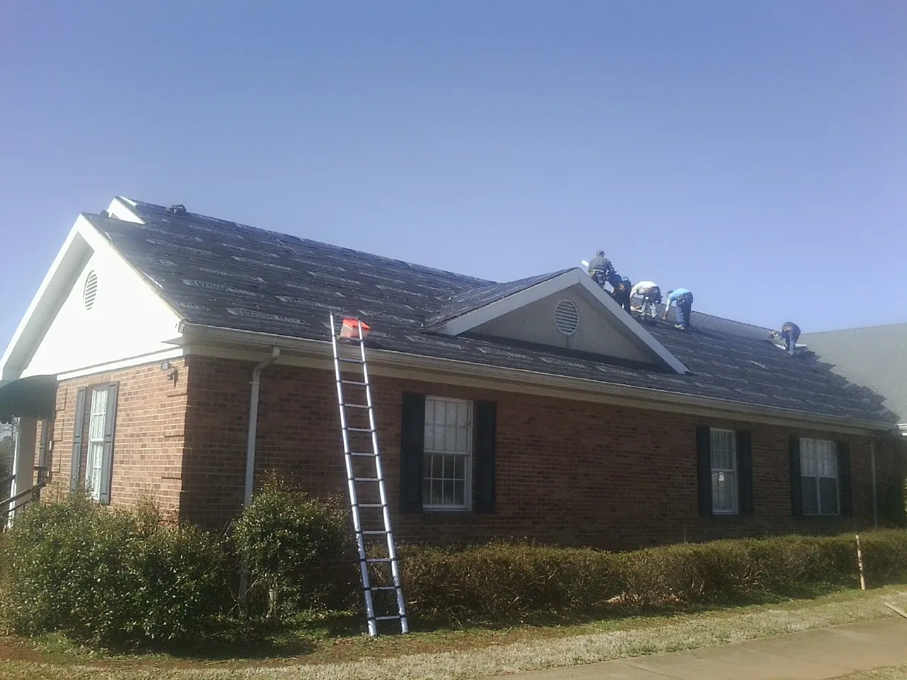 Crew tearing shingles off a brick ranch roof with a ladder set — Emergency Roof Repair work by our crew in Wareham