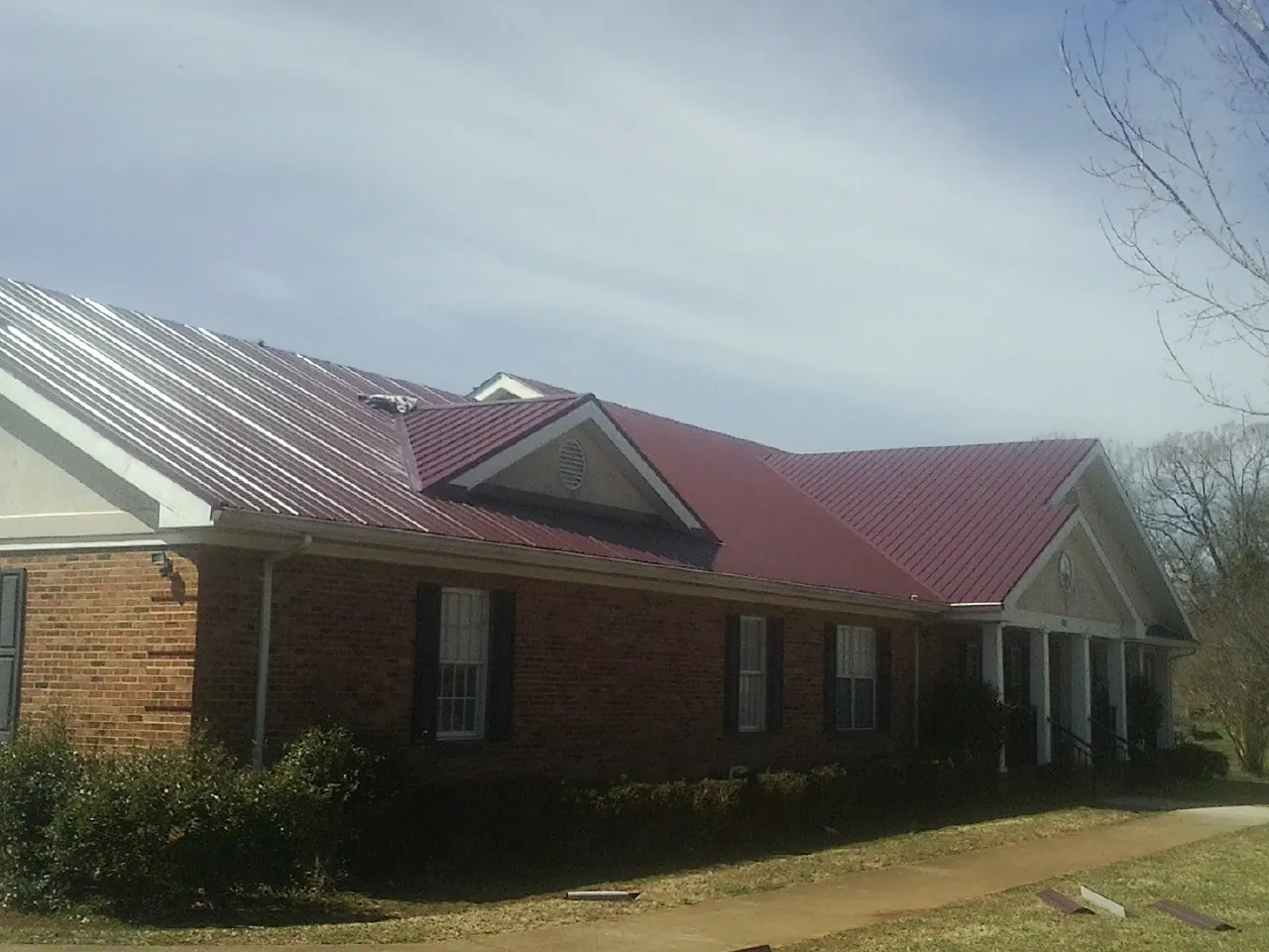 Red metal roof with gabled entries on a long brick building, from a Hail Damage Roof Repair job in Wareham