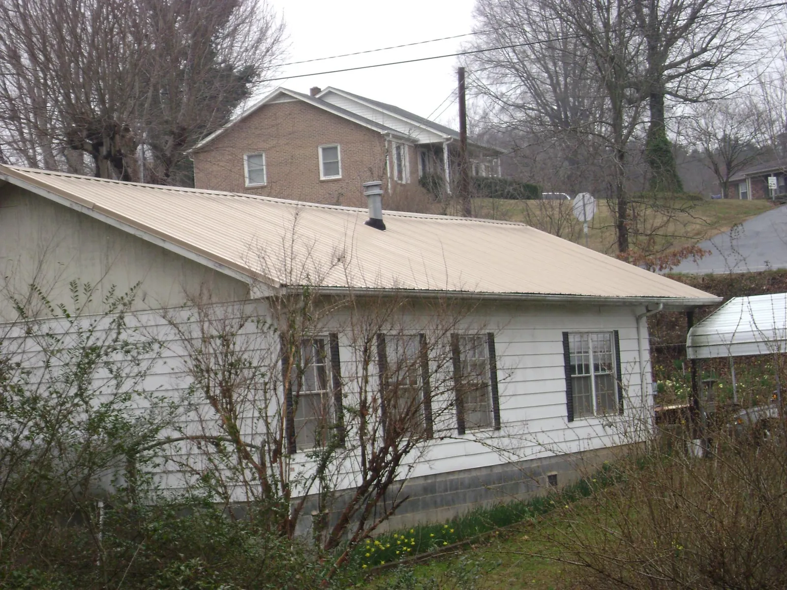 Tan metal roof on a white sided house set into a hillside — Commercial Roofing by Roofing Brothers in Wareham